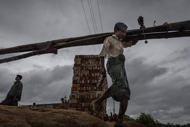 A man carries treated bamboo through a heavy downpour of rain to use to repair his damaged shelter. In early July 2019, the monsoon rains arrived with four days of continuous rain that destroyed 273 s...