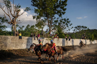 Child jockeys race past spectators, perched on a wall and even in trees, during a preliminary round of the 'Regional Police Chief's Cup 2019'.Racing is deeply rooted in the island's culture but the us...