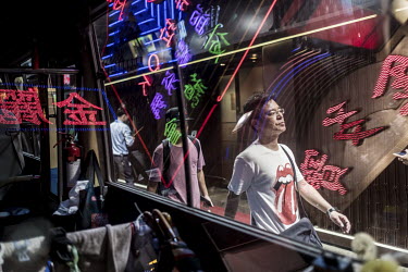 A pedestrian walks along Portland Street in Kowloon, as seen through a bus window with reflections of the street's many neon and LED lights. This part of the city is one of the last bastions of neon l...