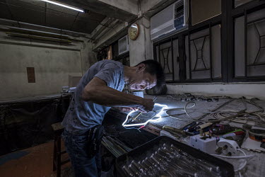 Choy Chun Wa (52) applies the final touches to part of a neon sign, painting a layer of black lacquer over certain sections to block them out, in Master Wong's workshop in Mong Kok. Wa and Master Wong...