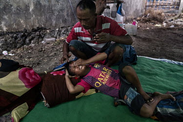 Abdul Gani (35) applies a herbal ointment to the wounds on his injured nephew Firmansyah's (8) face at a camp near the racecourse where they are based during the preliminary stages of the 'Regional Po...