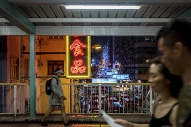 Pedestrians walk past a glowing neon sign on an overpass in Mong Kok.