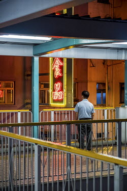 A man observes a glowing neon sign from an overpass in Mong Kok.