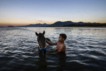 At dusk, after a day of racing in the 'Regional Police Chief Cup 2019', a boy washes a race horse in the sea, a task usually performed by former child jockeys and stable boys.   Racing is deeply roote...