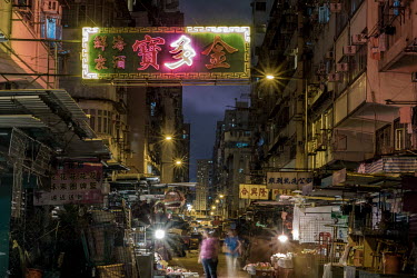 A single, flickering, half illuminated neon sign hangs above a street market on Canton Road in Mong Kok, Hong Kong.
