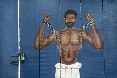 A painting of a chained slave at the gateway to the Ancestral Slave River Park. A bay where slaves, robbed from the interior, were able to wash for the last time before being branded and sold to Europ...
