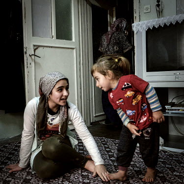 Syrian refugee Dalal Eissa (13) plays with a friend's daughter in her family's small apartment. Dalal's family work hard and send their young children out to work in a nearby factory so as to earn eno...
