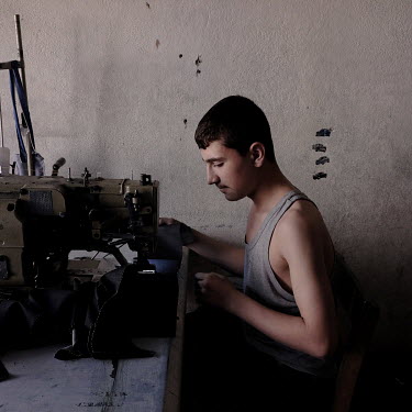 A young Syrian refugee works on a pair of jeans in a small factory employing Syrians who work longs hours for low wages.