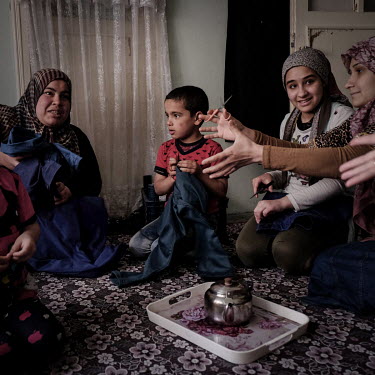Syrian refugees Wardeh (25, L), her son Farid, Dalal Eissa (13) and her mother Ayeesh cutting cotton threads from pairs of jeans which are made in a nearby factory. The meagre work pays 25 Turkish Lir...