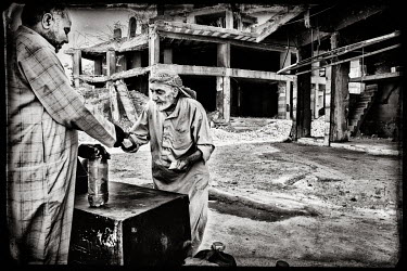 An elderly man selling low quality fuel on the street in a war damaged neighbourhood.