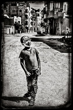 A boy in a spiderman mask walks through the war damaged streets.