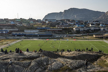 Sisimiut soccer stadium, an artificial pitch surrounded by metal fence between a road and a cliff used as a natural spectator stand.  The Greenland soccer league's season lasts less than a week, wit...