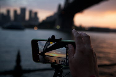A Chinese tourist on a bus tour, takes a photo using their mobile phone of The Sydney Harbour Bridge shortly before Sunset.