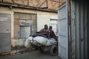 A disabled man at Onatra port, sits on a cart loaded with his wheelchair and sacks of imported goods. As disabled people pay less import fees savvy traders use them to import cargo cheaply from Congo...
