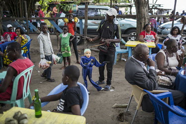 A puppeteer controls a marionette as he performs to customers in a cafe.  On weekends, Kinois flock to the river banks, to party, dance and drink. Musicians, puppeteers and acrobats seek to take adv...