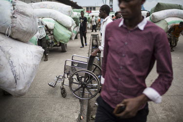 A man with a wheelchair stands among the carts loaded with imported goods at Onatra port. As disabled people pay less import fees savvy traders use them to import cargo cheaply from Congo Brazzaville....