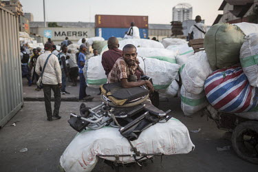 A disabled man at Onatra port, sits on a cart loaded with his wheelchair and sacks of imported goods. As disabled people pay less import fees savvy traders use them to import cargo cheaply from Congo...