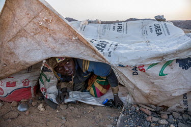 A man looks out from underneath a makeshift covering made out of old sacks near a large artisinal gold mine. The miners come from all over the country and live in very primitive conditions while worki...