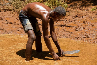 A man collects rain water from a muddy pool.