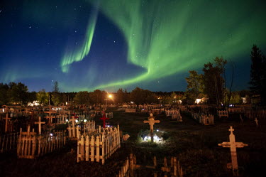 The northern lights (aurora borealis) glow green in the night sky above the main cemetery in Fort Chipewyan.
