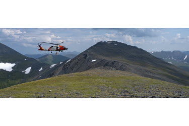 A member of a coastguard team is winched down from a Jay Hawk helicopter as it flies over the land near Kotzebue during a search and rescue exercise.