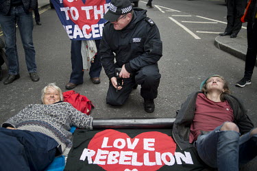 A policeman talks with two women joined together by a chain in a metal tube who are lying on the road surface during an Extinction Rebellion protest in Trafalgar Square.