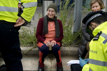 An activist who took part in non-violent direct action at London City Airport sits down after being arrested by the police.