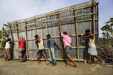 A group of men salvages a zinc metal sheet that once formed the side of a building, one of many that have collapsed as the rising waters of the Meghna River have swept away the unstable land that they...