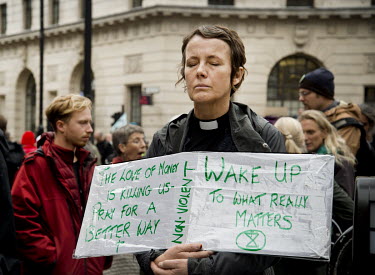 A vicar meditates while holding a sign during an Extinction Rebellion protest in Bank highlighting the impact that the financial sector's investment in fossil fuels, intensive farming and logging is h...