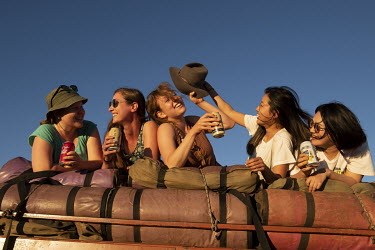 Backpackers lie on top of their equipment on the roof of a tour bus trailer, taking in the view of Uluru during sunset.   Tourists are rushing to climb world heritage-listed Monolith, Uluru in Austr...