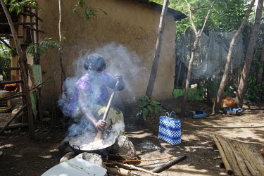 Farmer Poline Achieng stiring a metal dish of food cooking on an open fire.