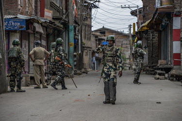 A member of an armed security personnal patrol films with a mobile phone as the group walk along a deserted street in the days following the Indian government's scrapping article 370.