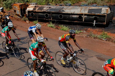 Cyclists on the Orodara - Bobo Dioulasso stage of the 'Tour du Faso' pass a burnt out fuel truck lying at the roadside.