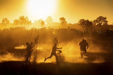A player from the home side, the Yuendumu Magpies, kicks the ball during a match being played at sunset during the Yuendumu Australian Rules Football Carnival.  Once a year Football teams from all o...