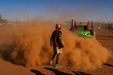 Red dust covers a spectator during a car show taking place shortly before the finals of the Yuendumu Australian Rules Football Carnival. Cars decorated in their team colours compete for the AUD 500 (G...