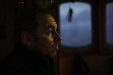 Janus, a fisherman, sits in the bridge of a boat during the night while fishing with his son Eivind and cousin Andrias.