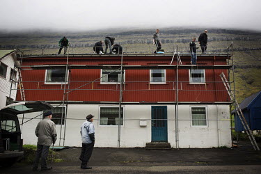 Men work on the roof and a scaffold to repair the top of a house in Hvannasund.