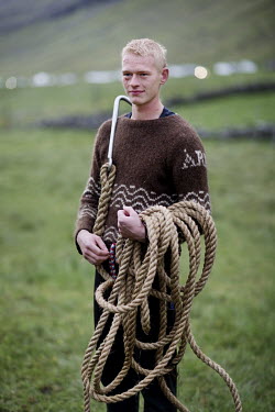 A young man carrying a rope and an anchor prepares to go whale hunting in Hvannasund.