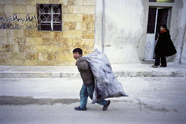 A Kurdish boy carrying a sack of rubbish for recycling in the Kurdish district of Sheikh Maksud.