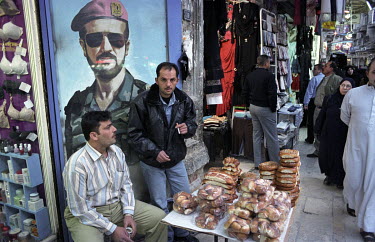 A mural portrait of Basil Al-Assad beside a man selling bread in Sharia al-Tilal, Al-Jdeida. From a young age, Basil was groomed to fill the role of President by his father, Hafez al-Assad, but he die...