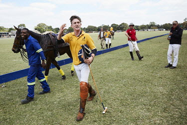 A polo player at the Lusaka Polo Club strides along the pitch with his horse and groom beside him.