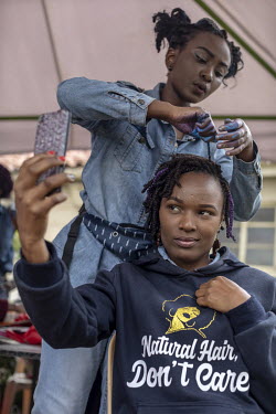 A woman takes a selfie as she has purple hair extensions attached by a hairdresser for 'Hairitage Chronicles. A festival for the Natural Hair Community'.