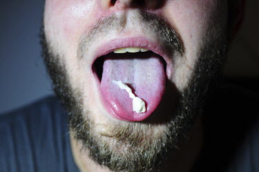 A man holds a bag containing the drug ecstasy on his tongue in order to hide it in his mouth.