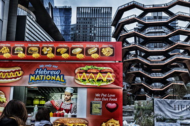 A Kosher foodtruck selling hot dogs serves customers from a pitch in front of the 'Vessel', a temporary name given to a honeycomb-shaped structure made up of linked walkways sited on Manhattan's West...
