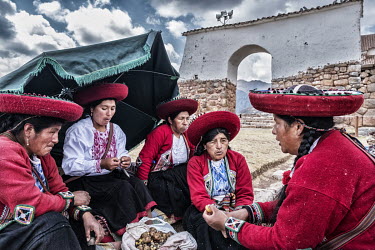 Indigenous women sitting near a Spanish colonial-era church while eating freeze-dried potatos for their lunch.