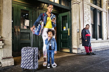 A mother and child wait with their luggage at a subway station.