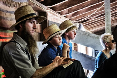 An Amish man and his children watch the sales at an auction where lots include small animals, foodstuffs, lumber, baby buggies and lawnmowers.