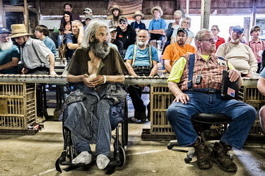 A disabled man sits in a wheelchair among a crowd that includes a large number from the local Amish community at an auctioneer's sale.