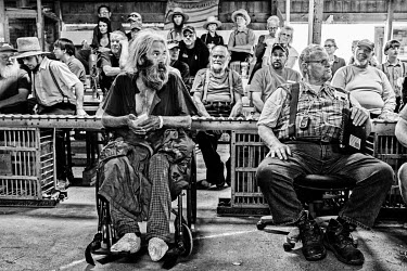 A disabled man sits in a wheelchair among a crowd that includes a large number from the local Amish community at an auctioneer's sale.