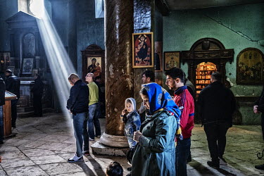 A beam of sunlight enters an Orthodox Christian church, illumibating a man at prayer.